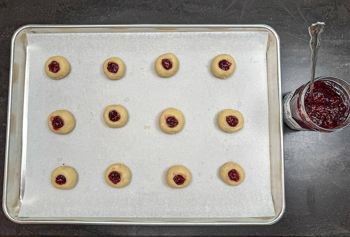 A pan with 12 cookies that are filled with preserves and ready for the oven.