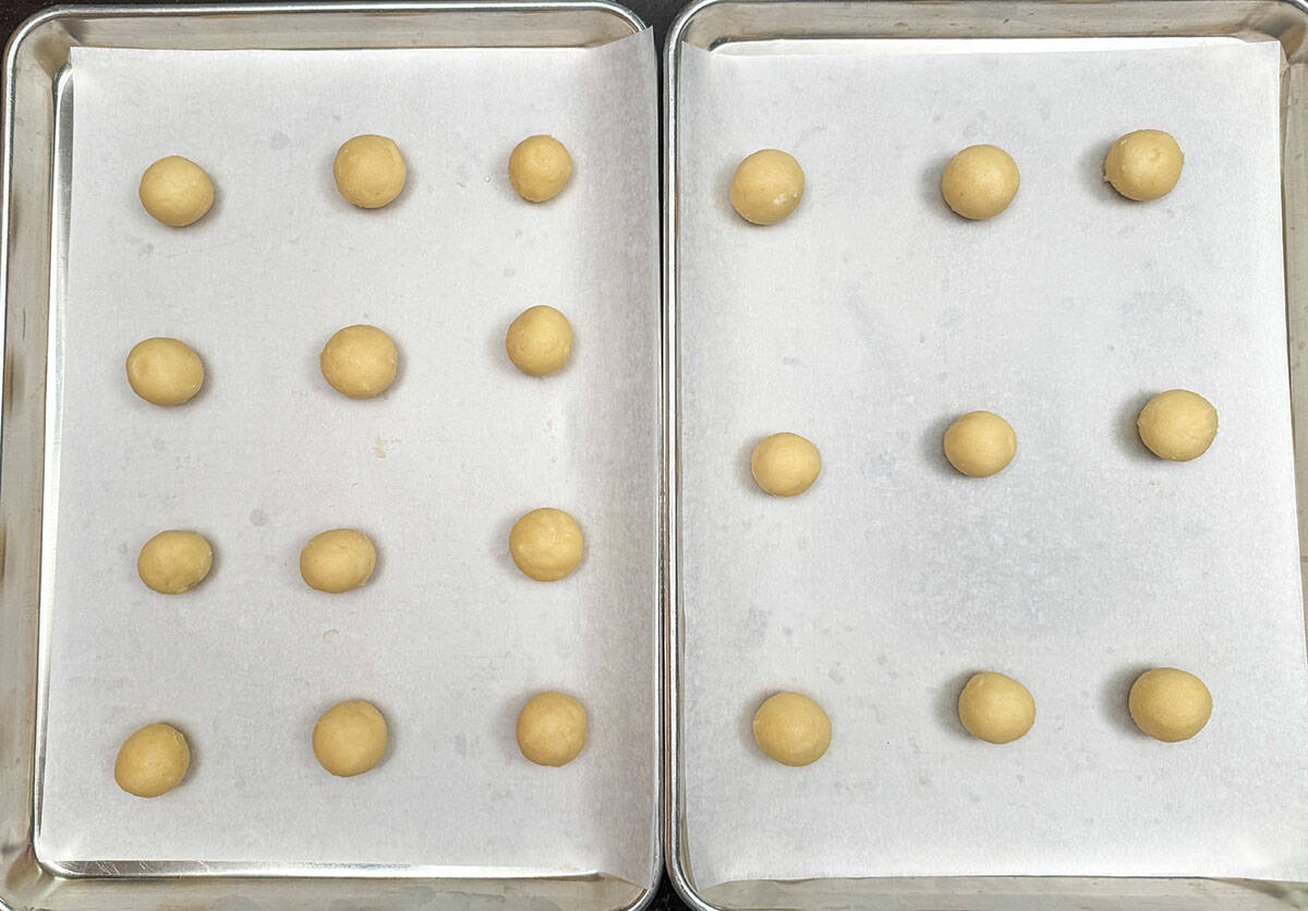 Twenty-one cookie balls on two sheet parchment lined sheet pans.