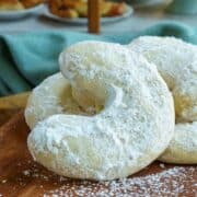 Amaretto almond crescent cookies on a wooden board in front of a bakery. Feature image.