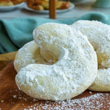 Amaretto almond crescent cookies on a wooden board in front of a bakery. Feature image.