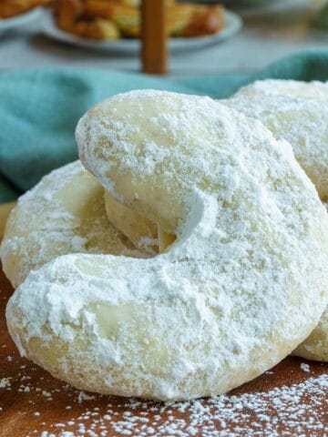Amaretto almond crescent cookies on a wooden board in front of a bakery. Feature image.
