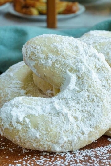 Amaretto almond crescent cookies on a wooden board in front of a bakery. Feature image.