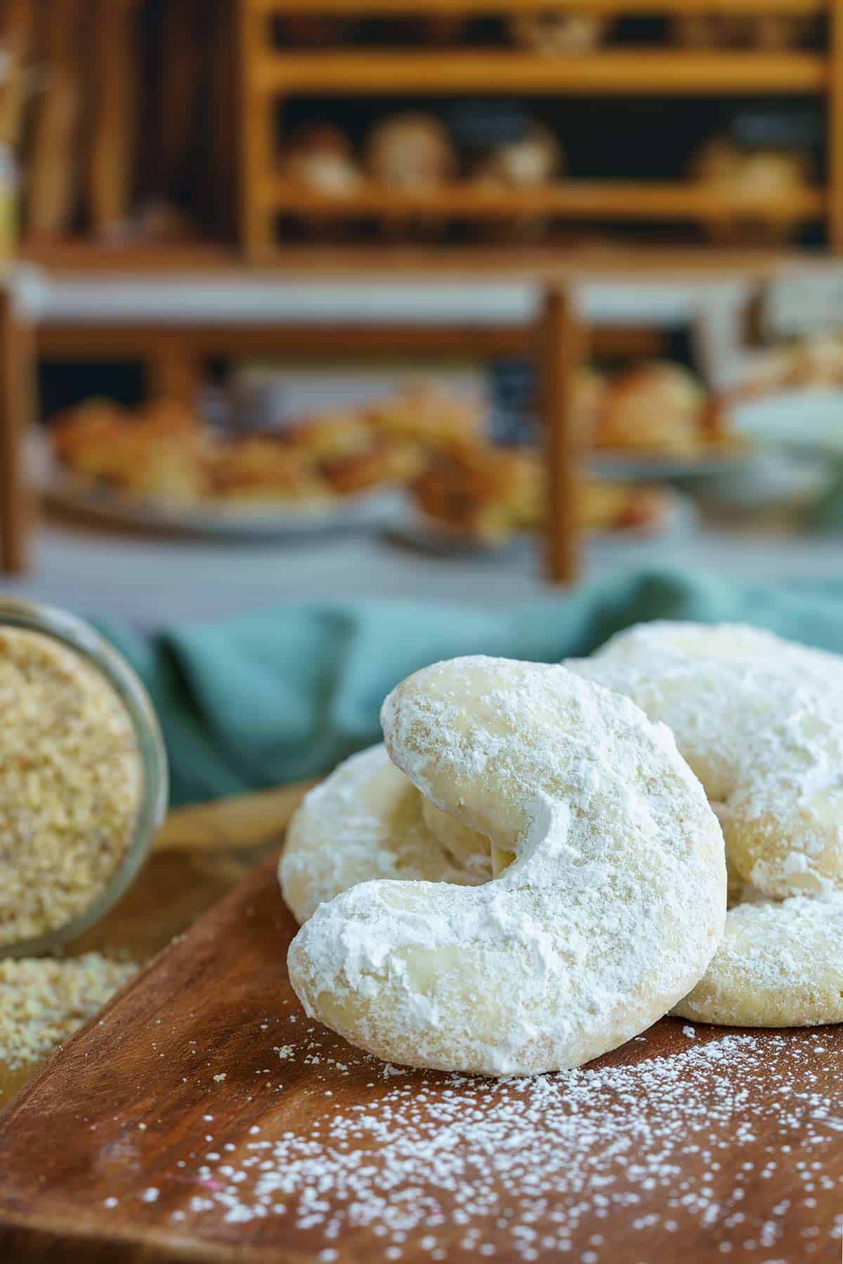 Amaretto almond crescent cookies on a wooden board in front of a bakery. Feature image long.
