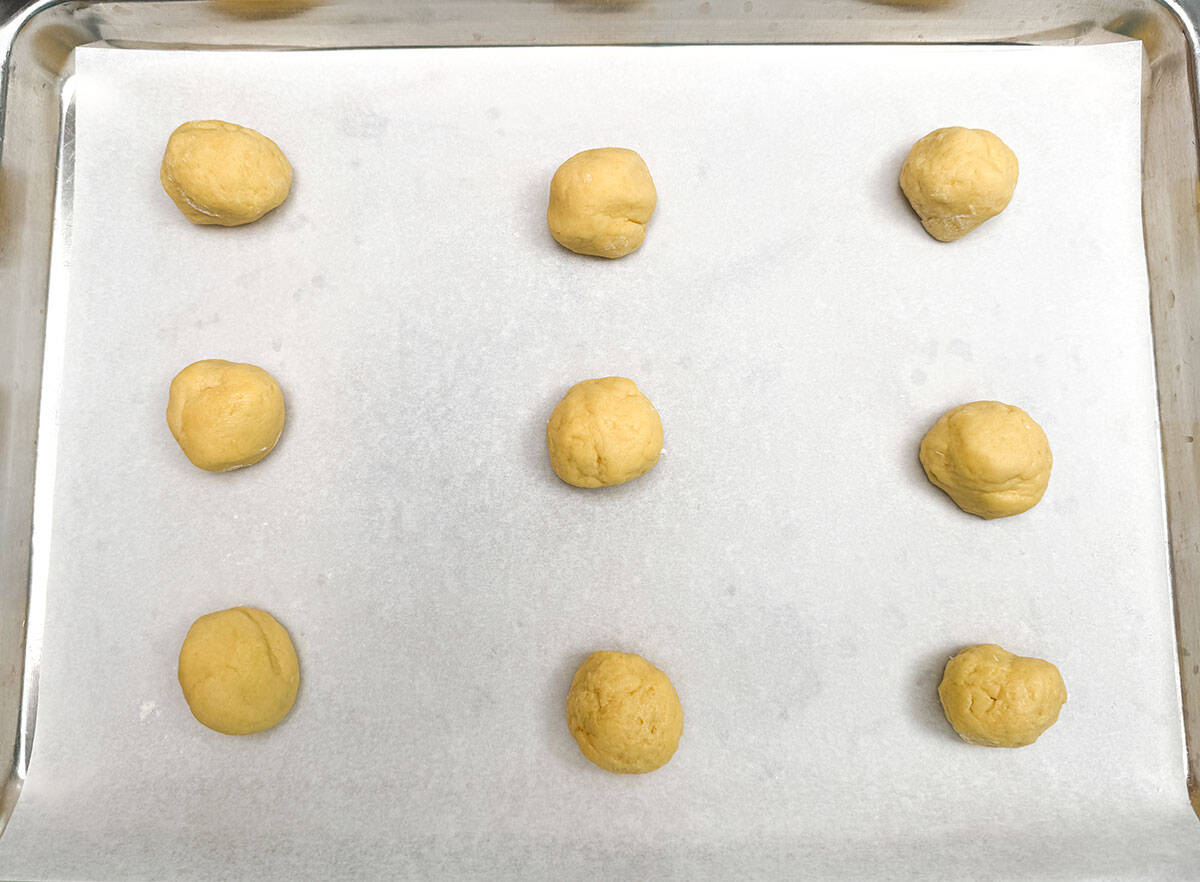 Nine cookie balls on a sheet pan ready to be baked.