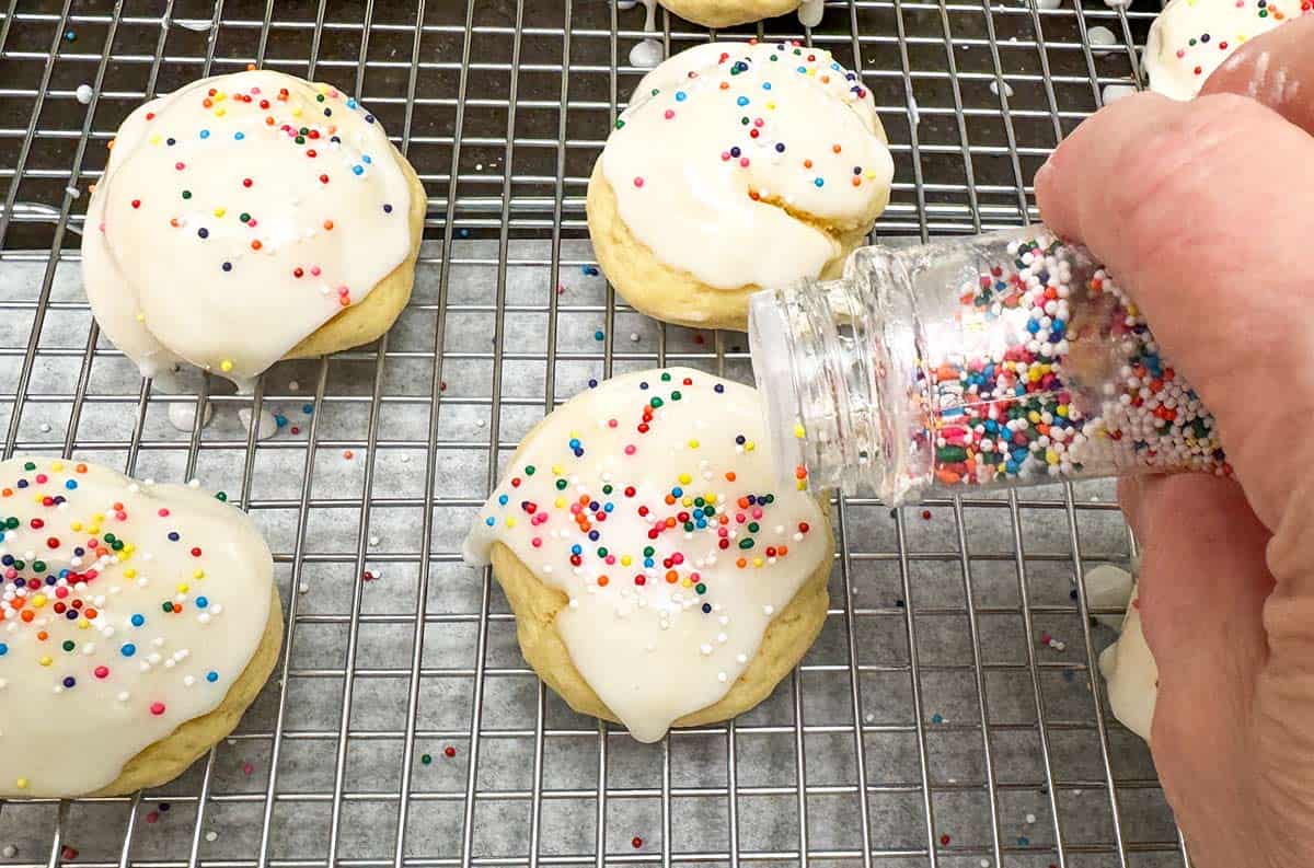 Adding nonpareil sprinkles to the icing on top of the cookies.