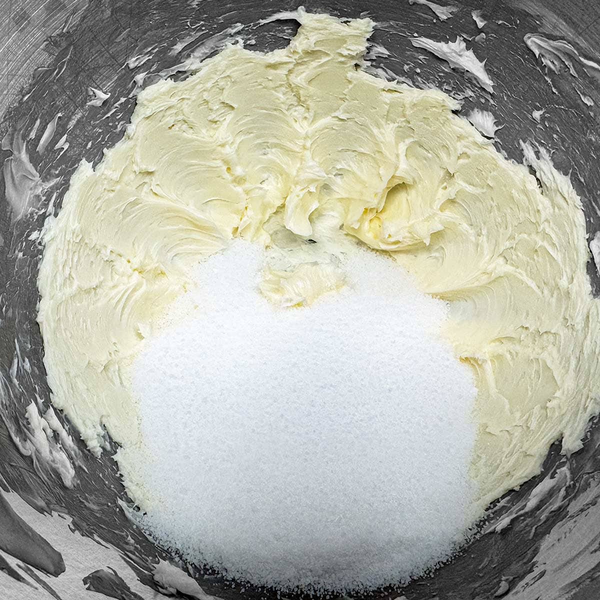 Adding sugar to the creamed butter in the mixer bowl.