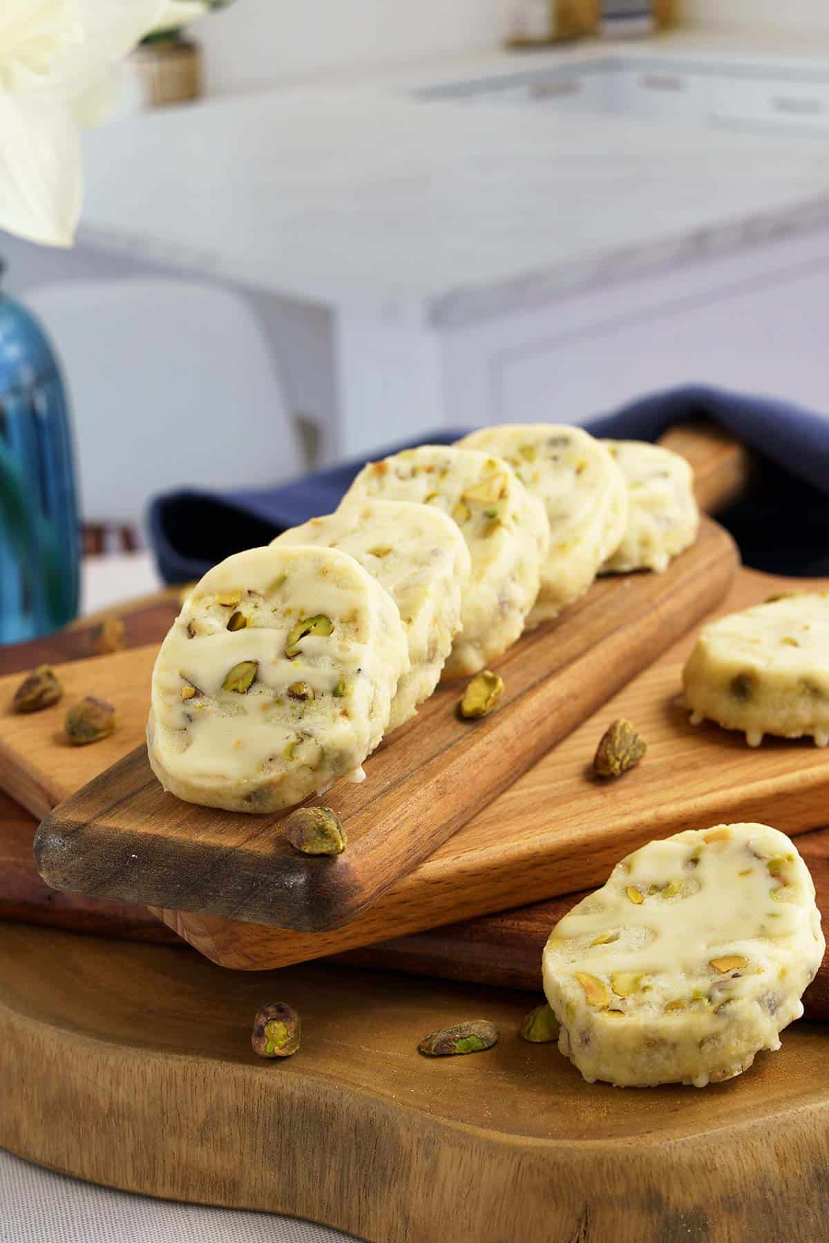 A side view of ¾ thick baked lemon pistachio cookies on a wooden board.