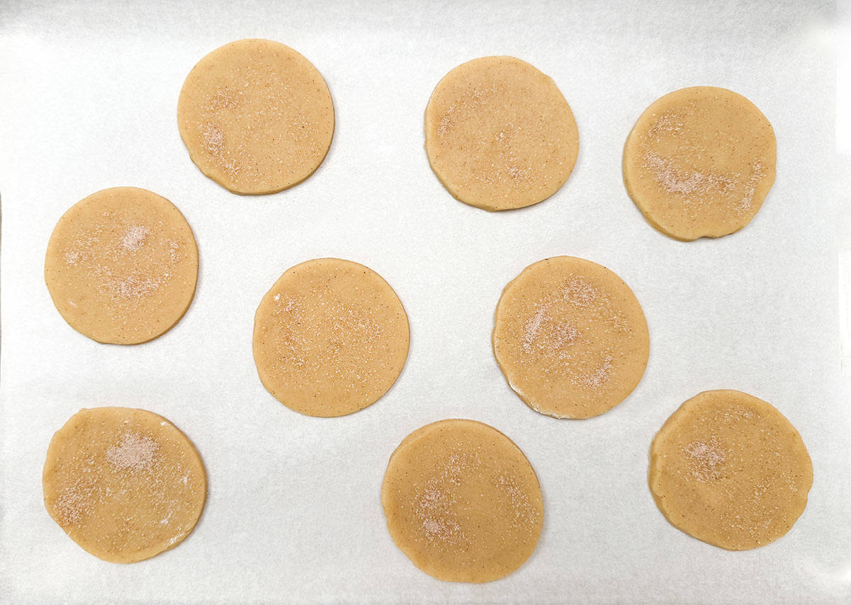 Cookies cut in circles on parchment paper with cinnamon sugar sprinkled on top ready for the oven.