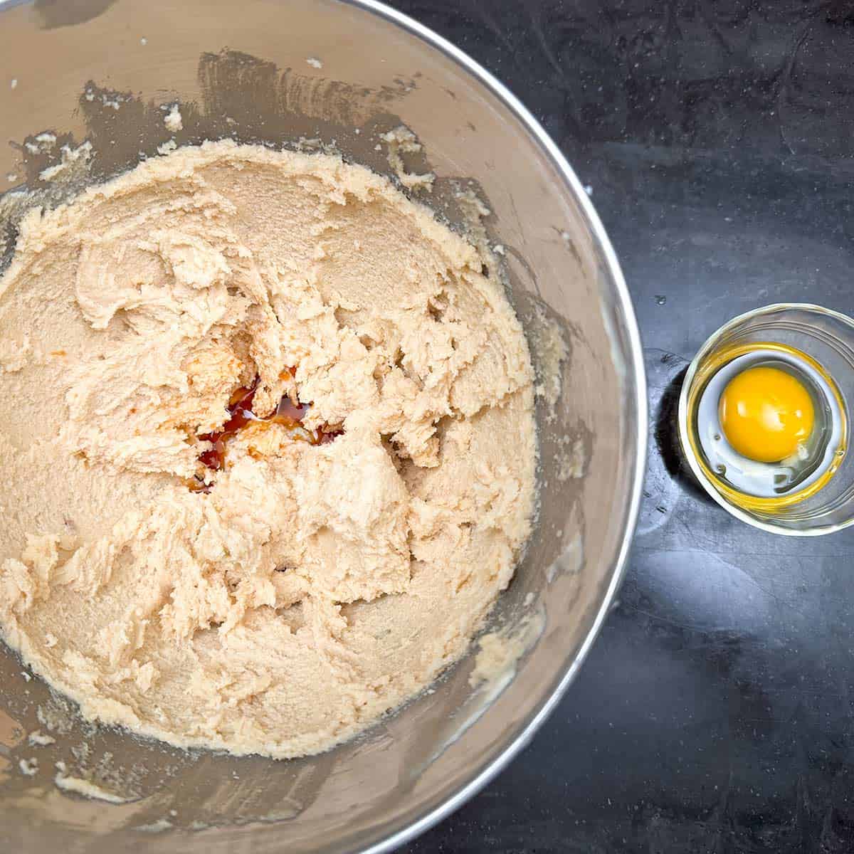 Vanilla extract in the butter-sugar mixture with a cracked egg in a small bowl on the side getting ready to be added.