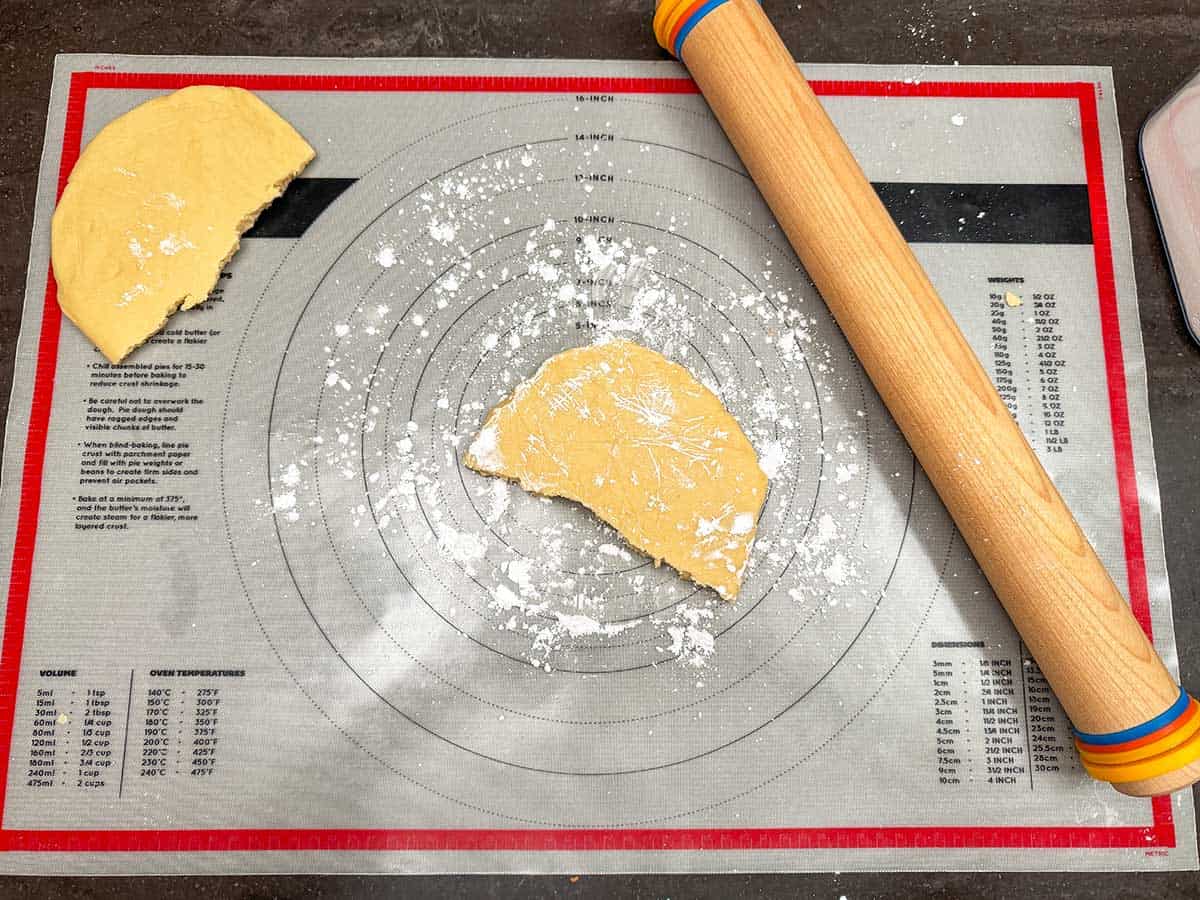 Cookie dough disk cut in half and on pastry sheet with rolling pin.