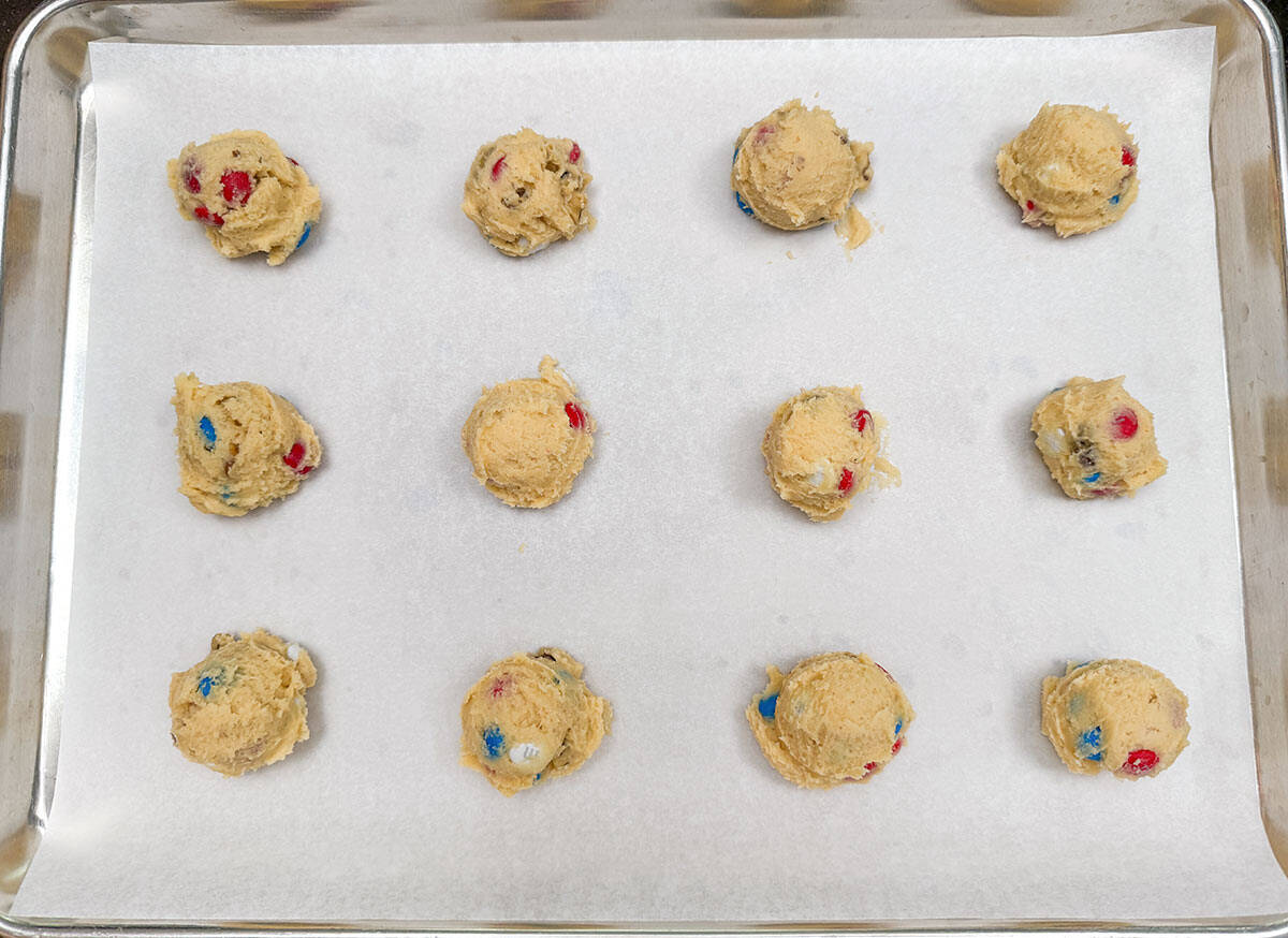 Red white and blue MM are peeking out of the scooped cookie balls on parchment lined sheet pan.