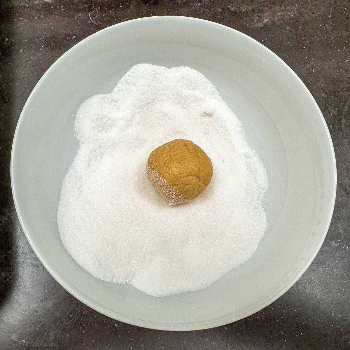 Cookie dough that has been rolled and added to a bowl of sugar to coat.