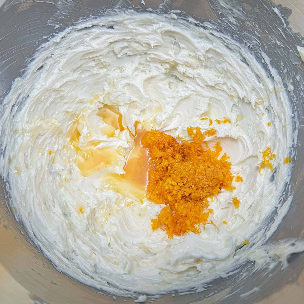 Adding orange juice and zest to the butter sugar mixture that is in a mixer bowl.