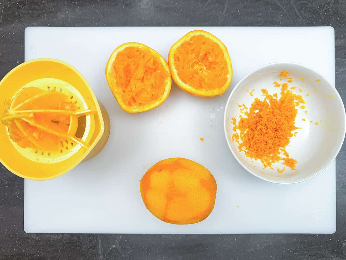 Zesting and juicing 2 oranges on a cutting board.