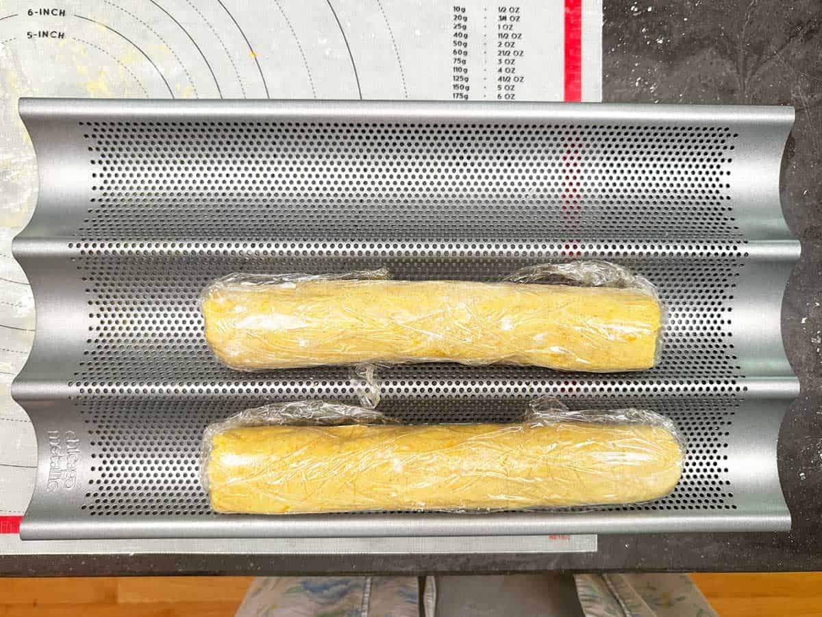 Two cookie logs wrapped and chilling in a baguette pan.