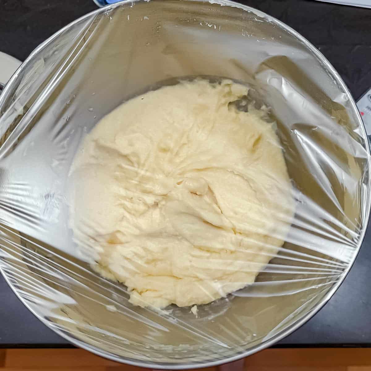 Cookie dough in bowl that has been covered with plastic wrap to go into the refrigerator.