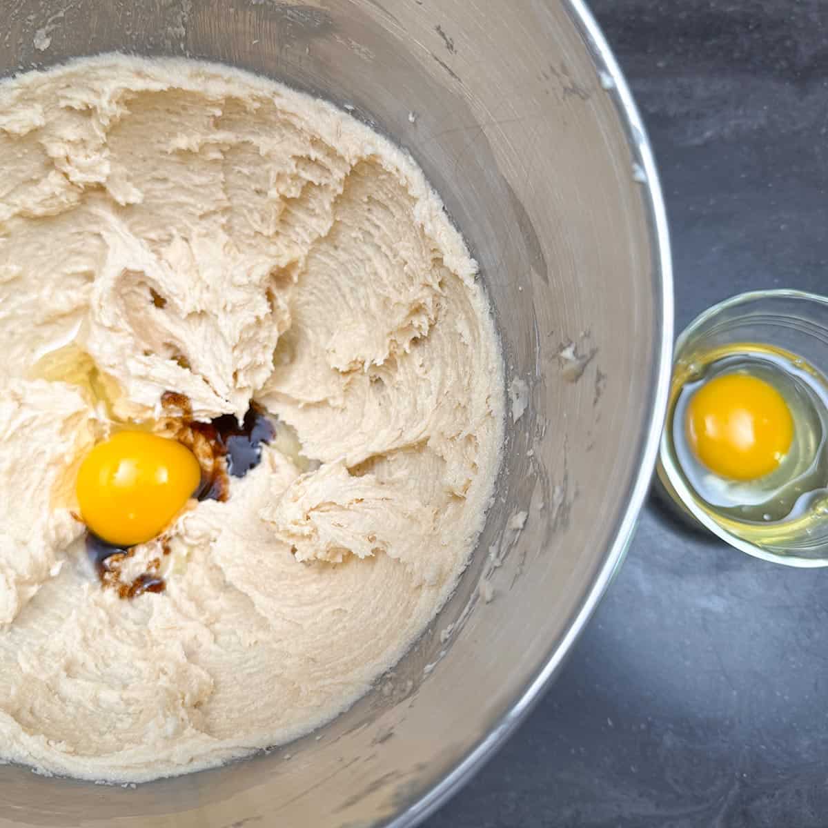 Adding eggs and vanilla bean paste to butter-sugar mixture in a mixer bowl.