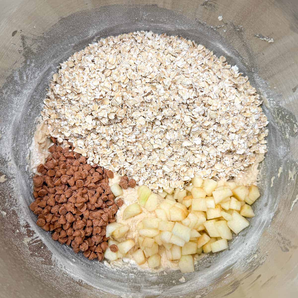 Adding oatmeal, caramel chips, and diced apples to cookie dough.