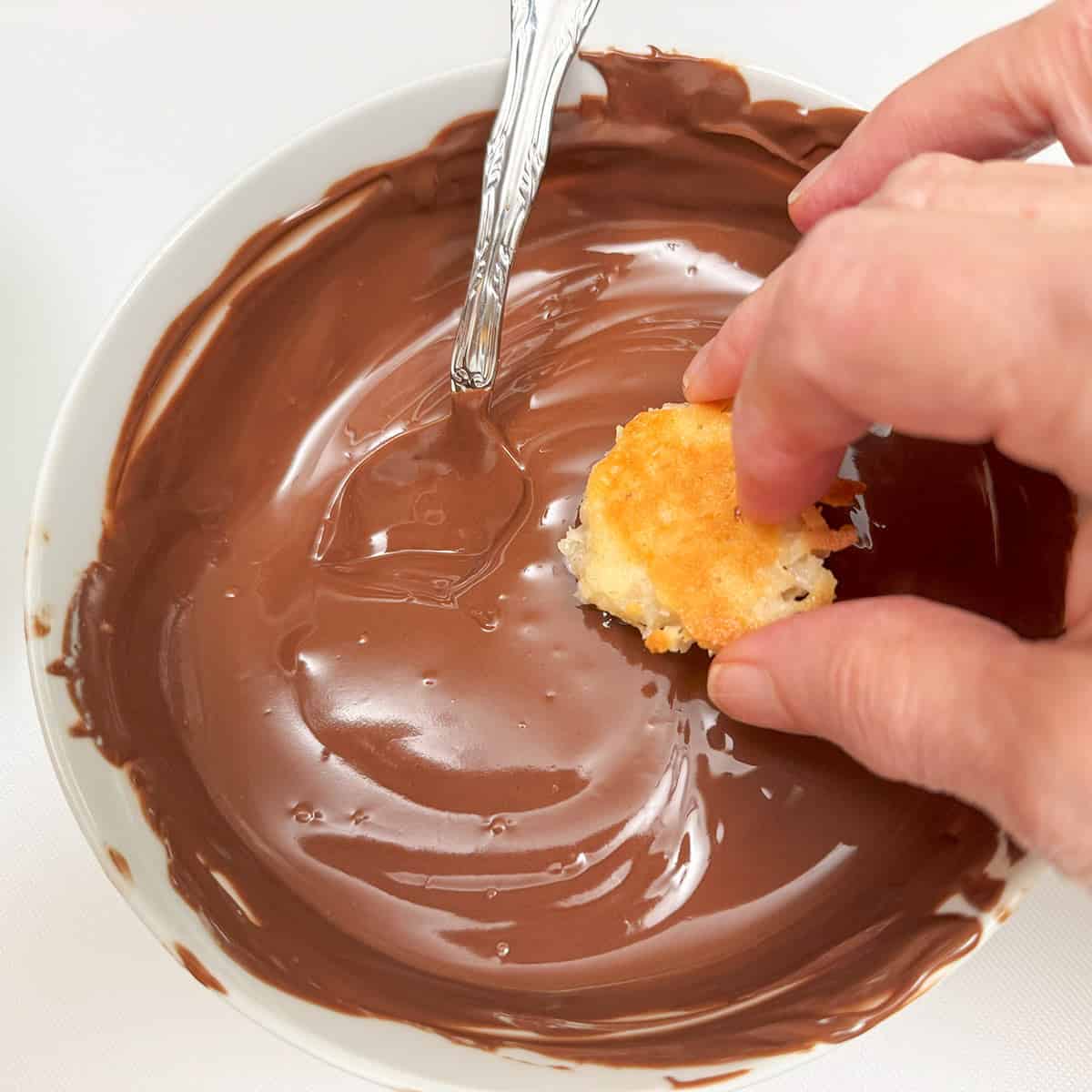 Dipping the tops of the macaroon in melted chocolate.