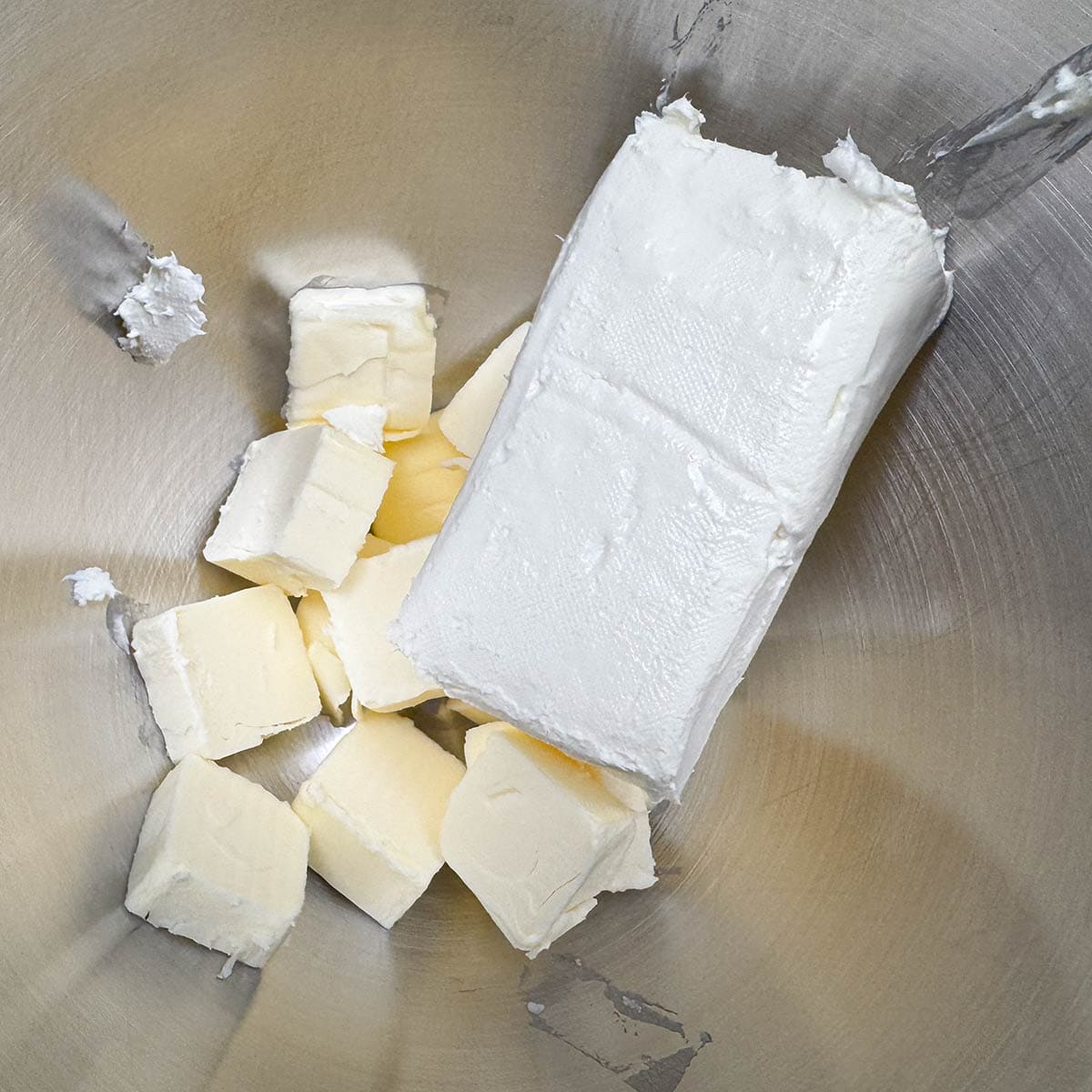 Cubed butter with a block of cream cheese in a mixer bowl.