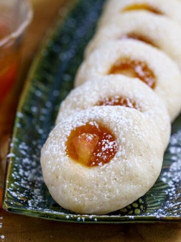 Fresh peach and preserves thumbprint cookies lined up on a narrow plate.