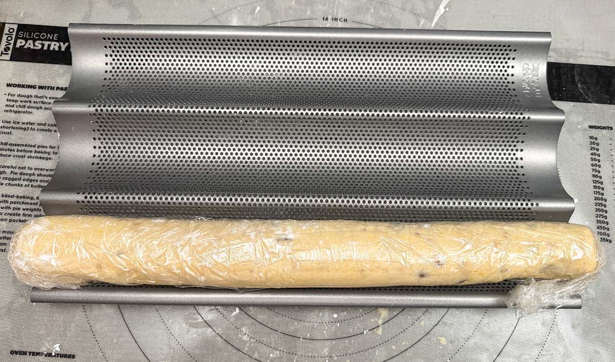 Wrapped cookie log resting in a baguette pan and ready for the refrigerator.