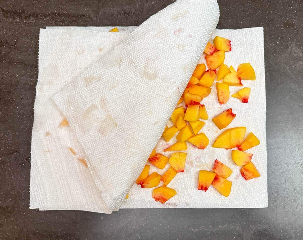 Peaches cut up and laying on paper towels to absorb juice along with dabbing paper towels on top.