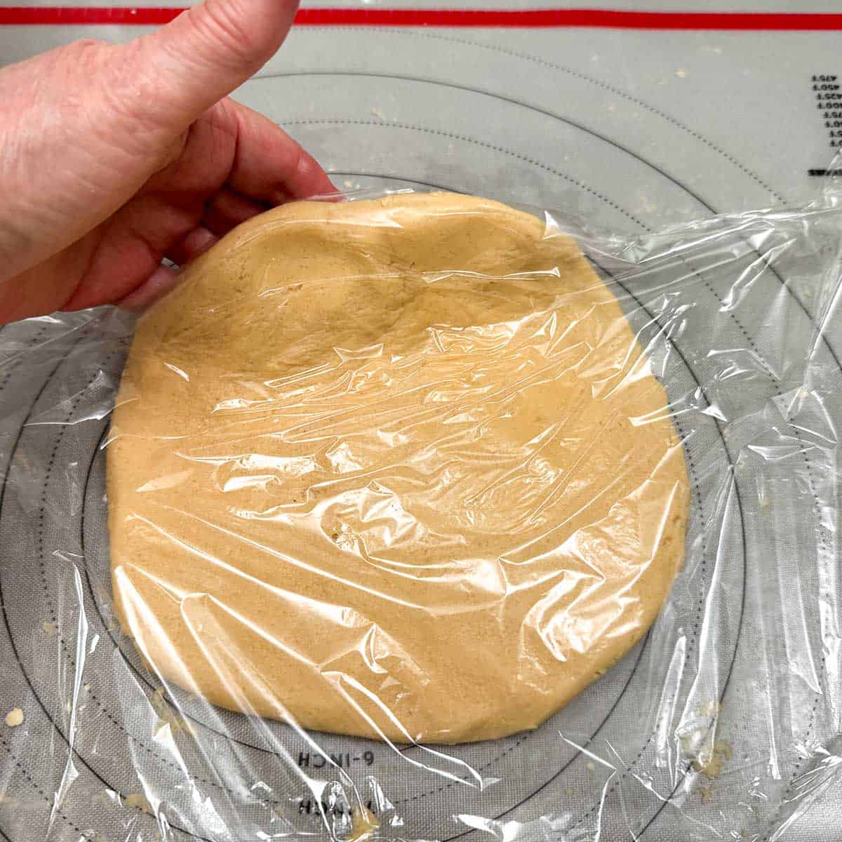 Lay plastic wrap on top of flatten cookie dough, lift and tuck wrap then pull up and flip over to finish wrapping.