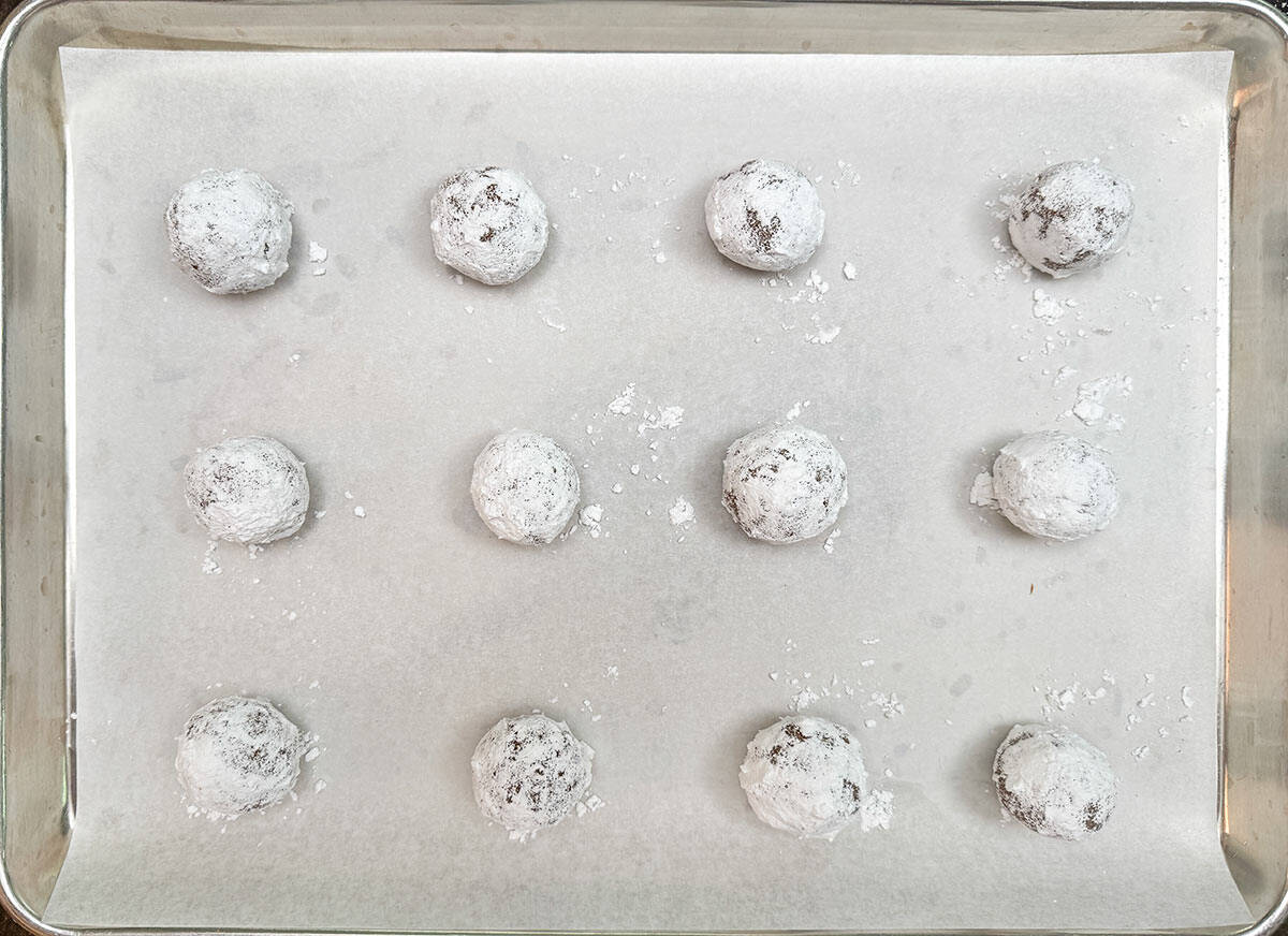 Sugar coated cookie balls on sheet pan with parchment paper and ready for the oven.