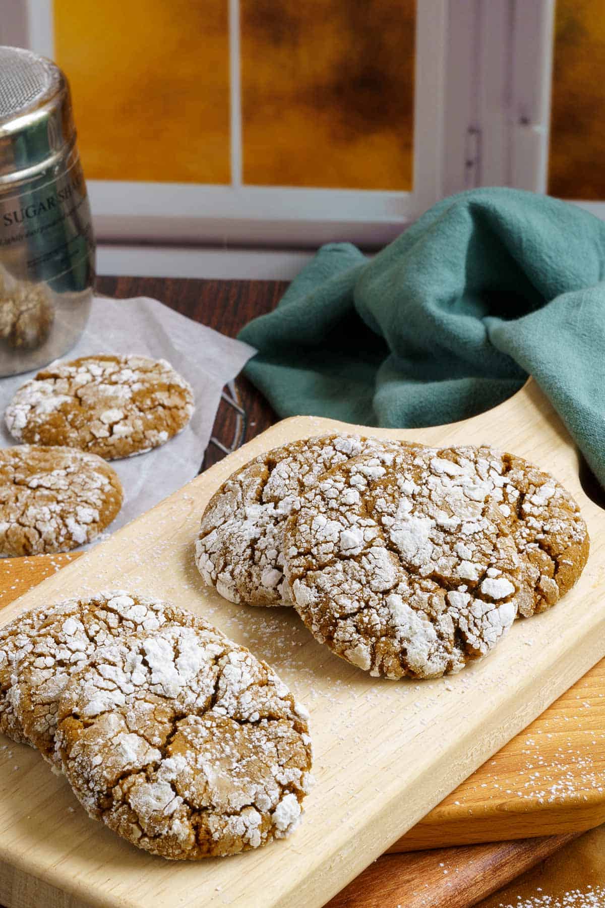 Eight gingerbread crinkle cookies on a wooden board in front of a window.