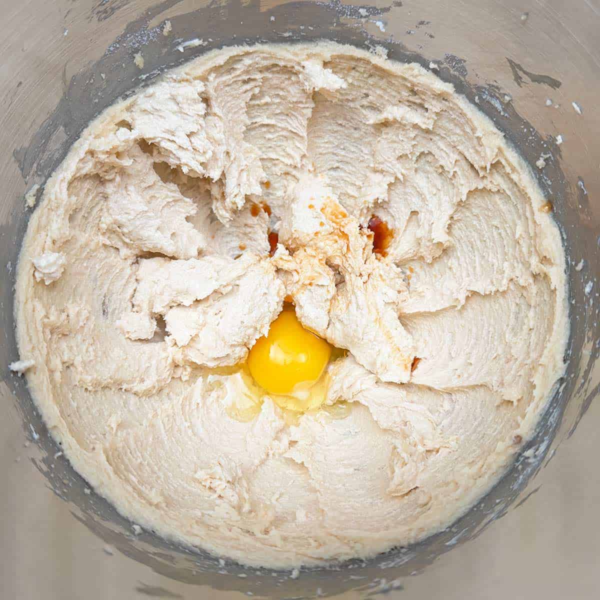 Adding an egg and vanilla extract to the butter-sugar mixture.