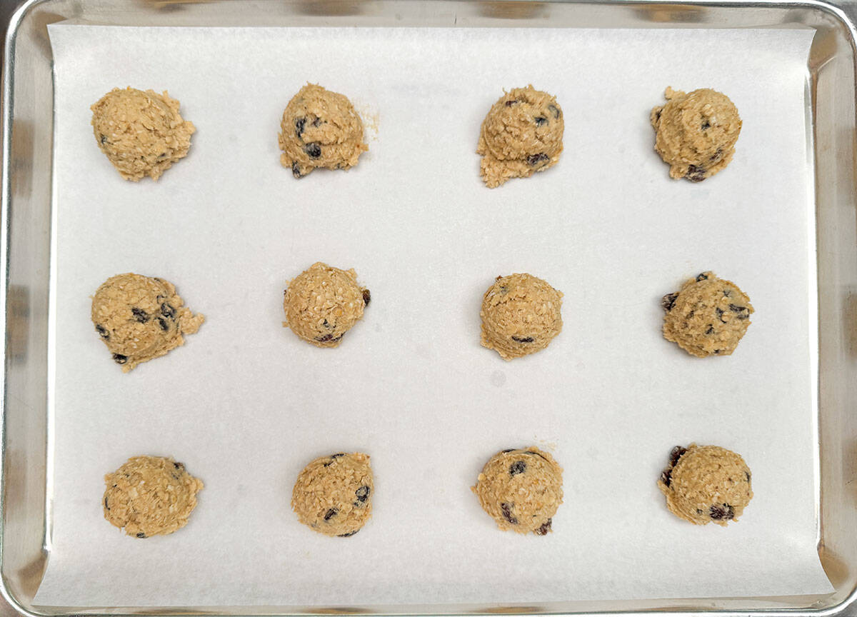 Oatmeal cookies scooped and on a parchment-lined cookie sheet pan.