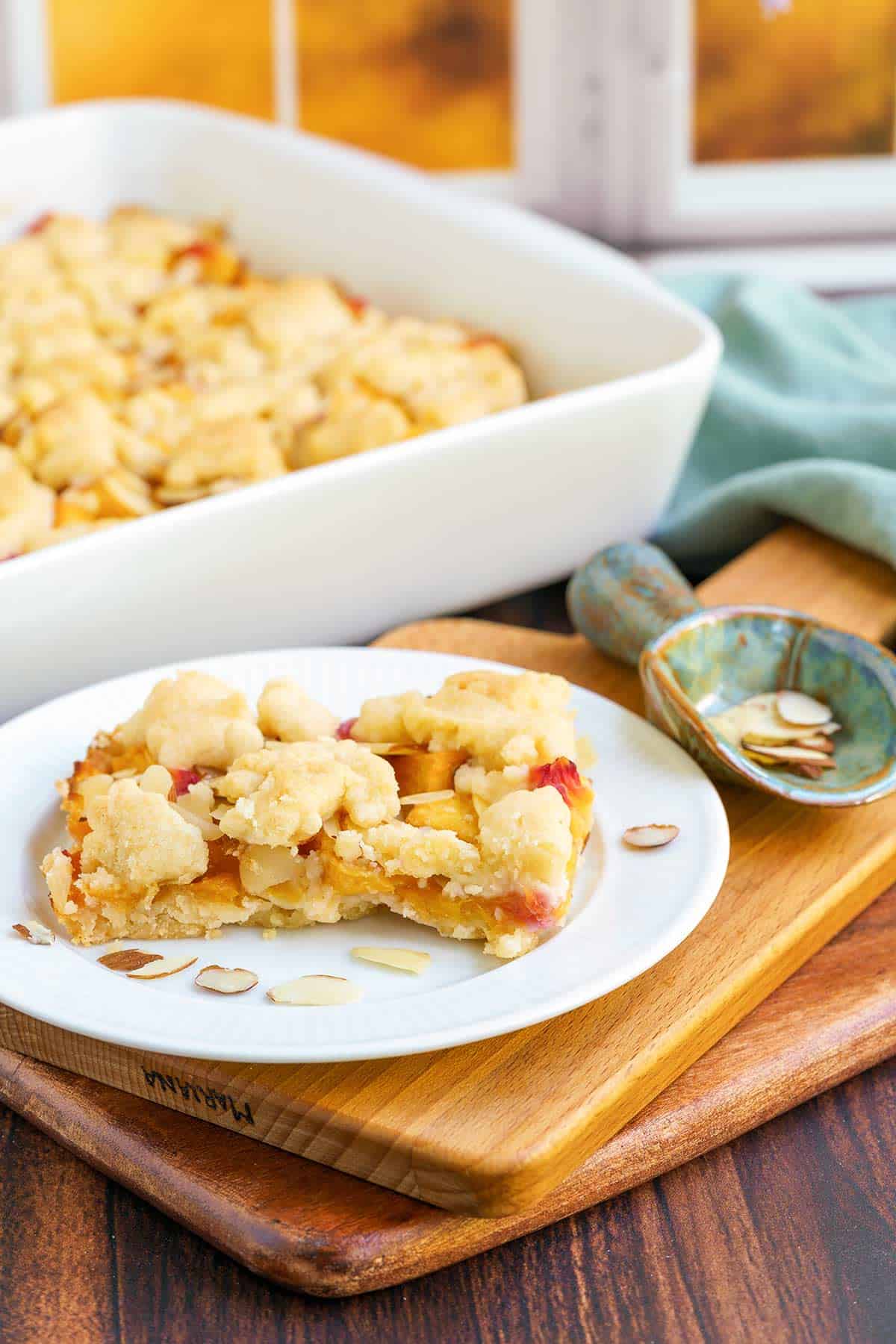A slice of Peach almond shortbread bars on a plate in front of a window.