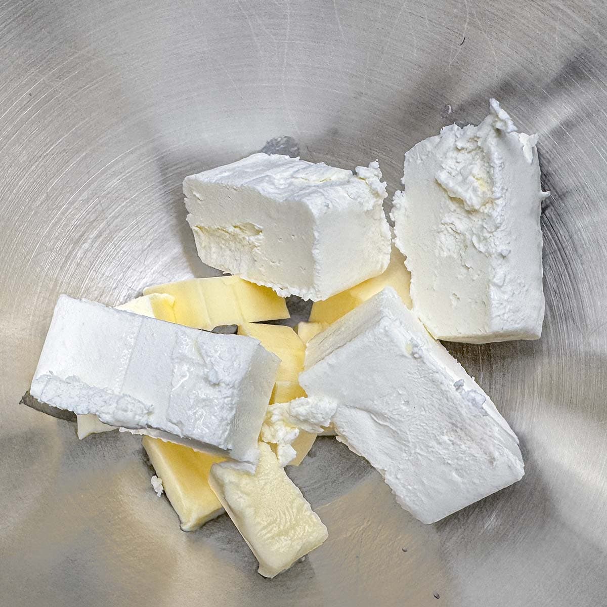 Cream cheese blocks with cubed butter in a mixer bowl.