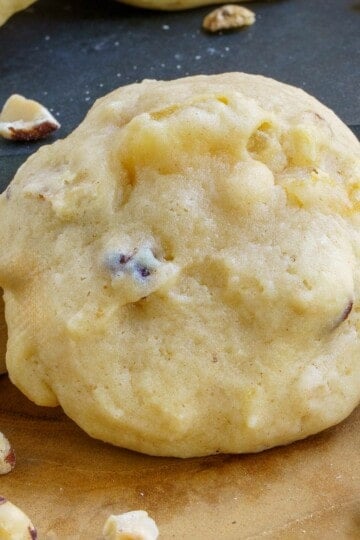 A Pear and Hazelnut cookie from a front view with hazelnuts around the board it is sitting on.