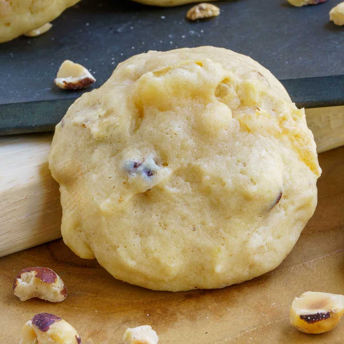 A Pear and Hazelnut cookie from a front view with hazelnuts around the board it is sitting on.