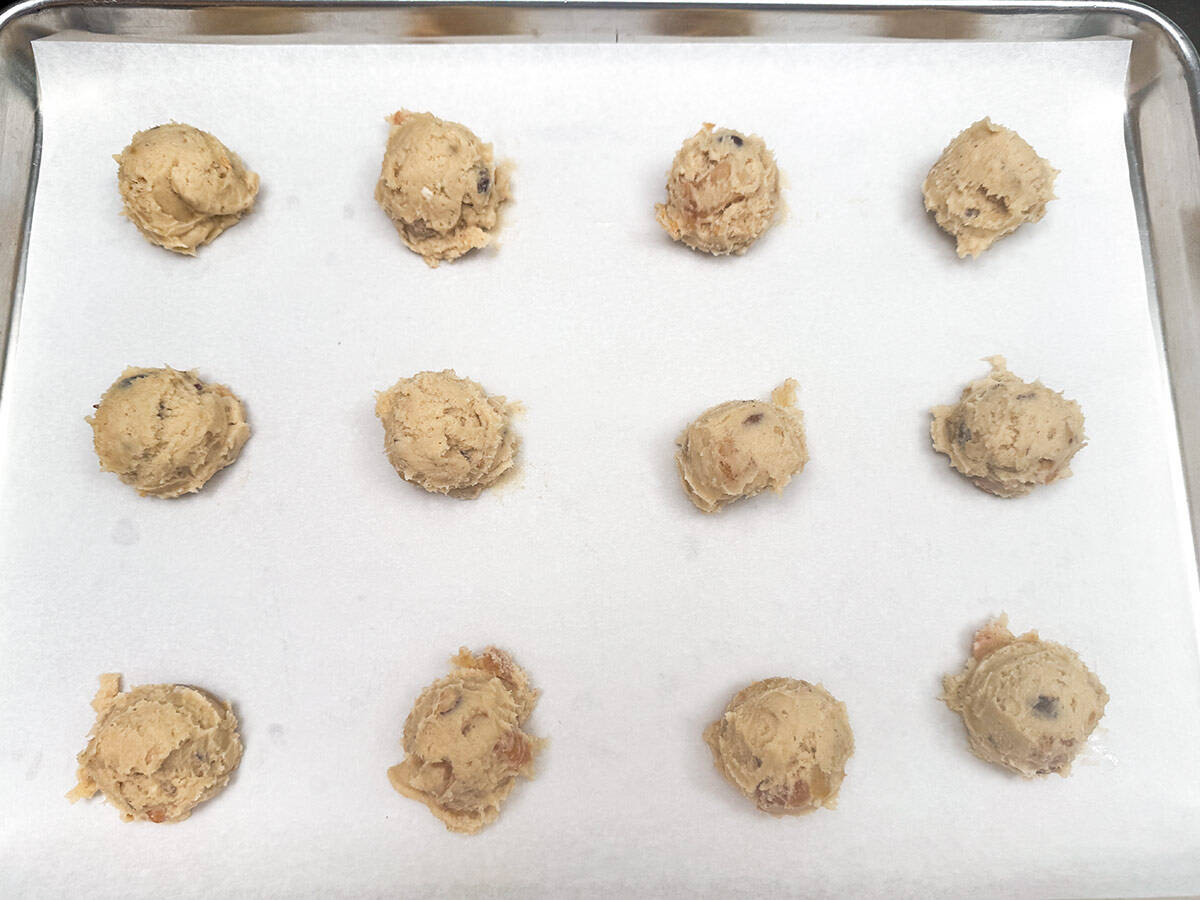 Twelve scooped cookie dough on a parchment-lined cookie sheet pan.