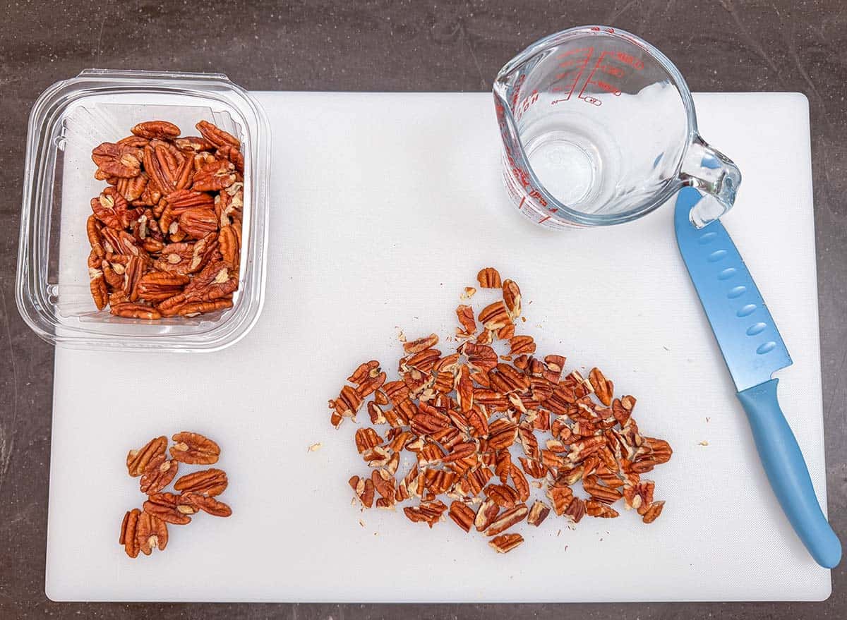 Pecan halves on a cutting board being chopped into smaller pieces.