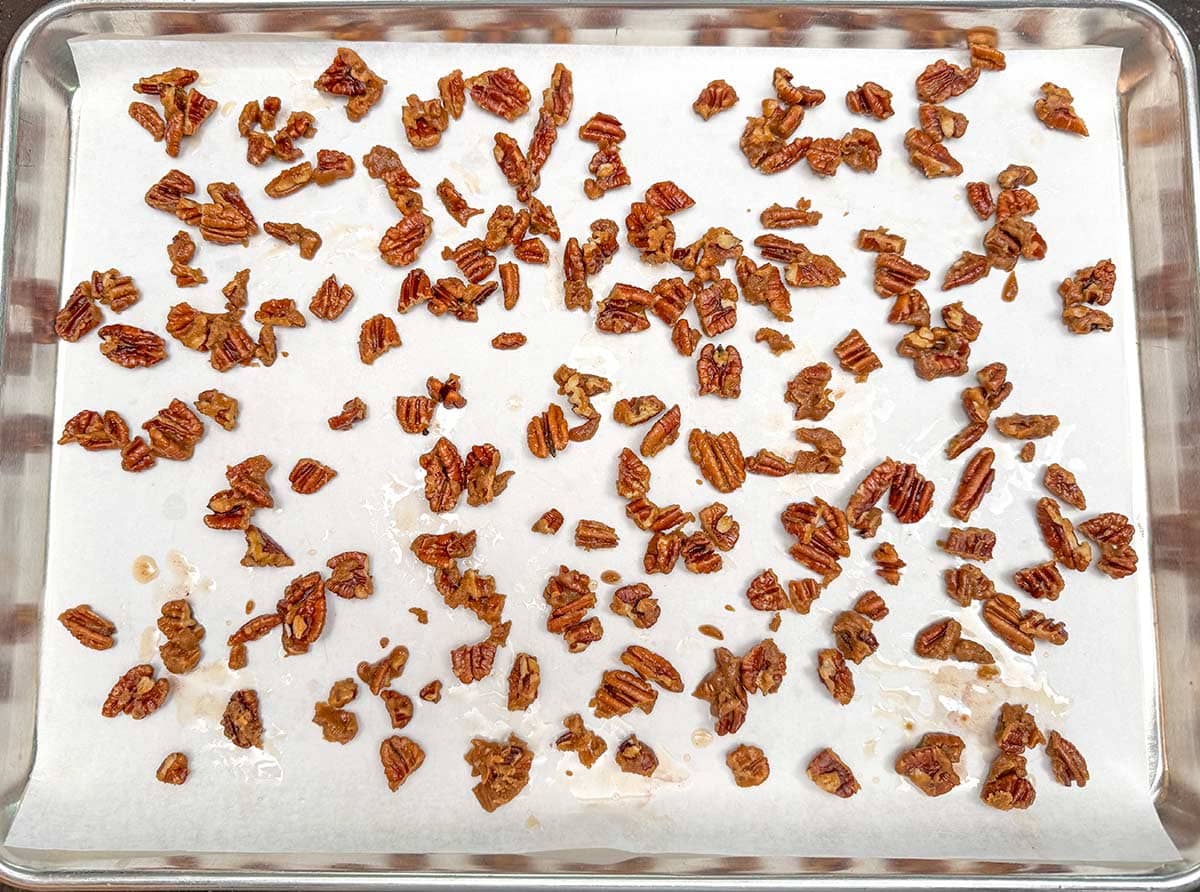 Glazed pecans cooling on a parchment lined sheet pan.