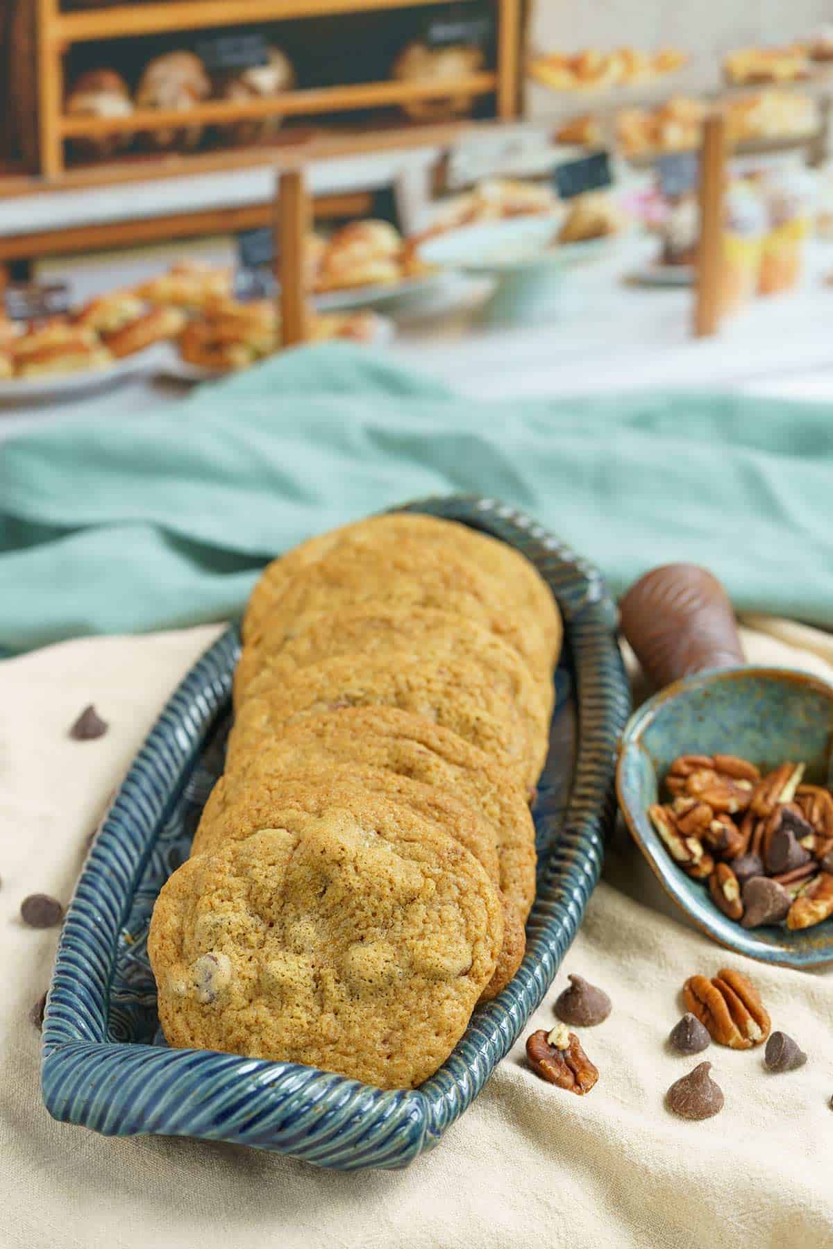 Chocolate chips with glazed pecans cookies in a log dish with chips and pecans laying around.