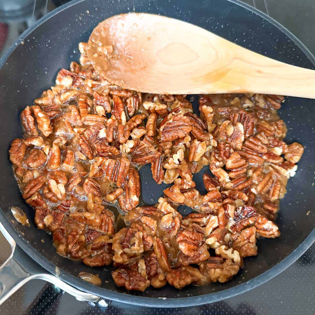 Stirring pecan pieces around the hot glaze in a small frying pan.