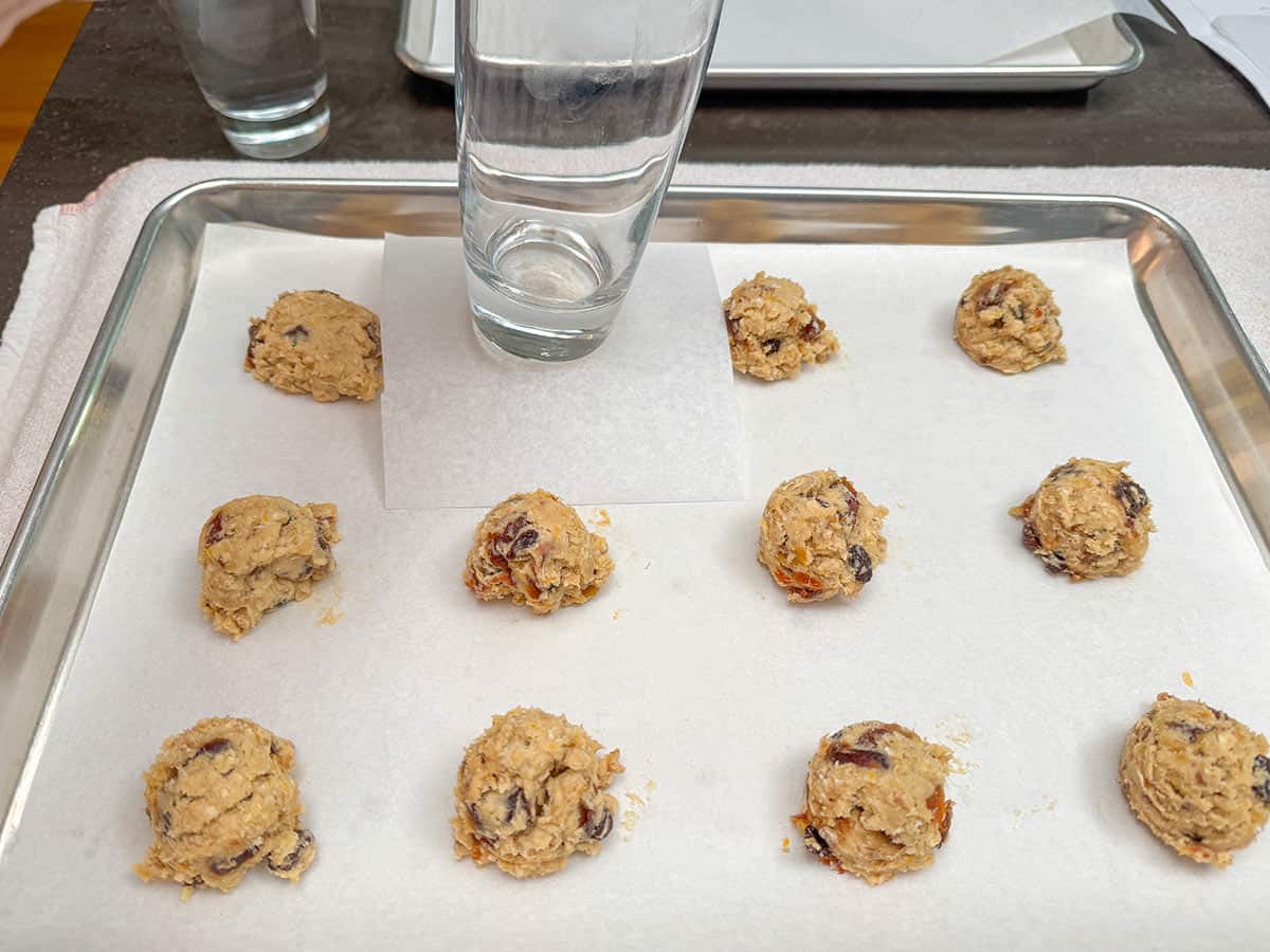 A glass bottom and a piece of parchment paper over a scooped cookie dough to flatten a little.