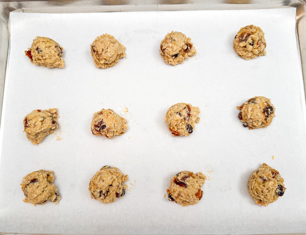 Twelve scoops of cookie dough on a parchment paper lined sheet pan.