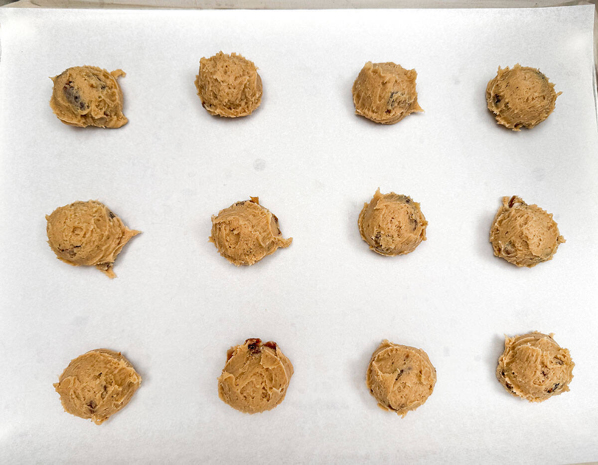 Cookie dough that has been scooped and on a parchment paper lined sheet pan.