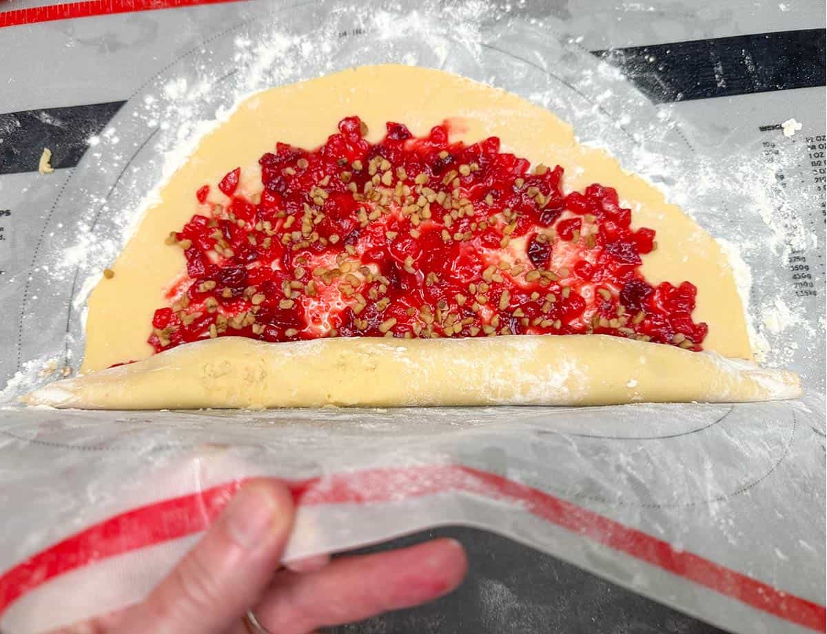 Lifting the pastry mat to help roll the dough into a filled log.