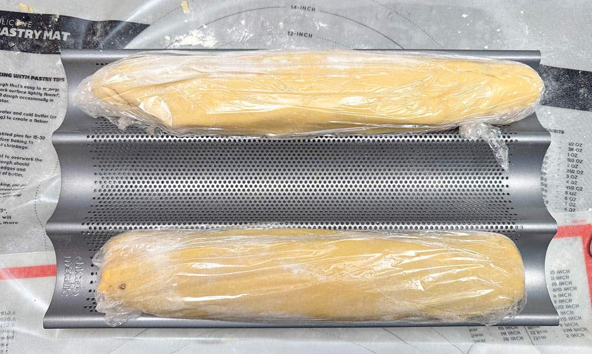 Both logs filled and wrapped in plastic wrap sitting in a baguette pan to hold the shape.