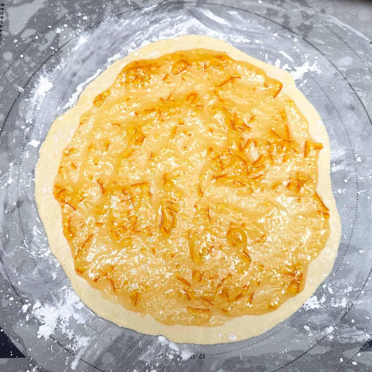 Rolled out cookie dough with the first layer of orange marmalade spread around within an inch of the outside rim.