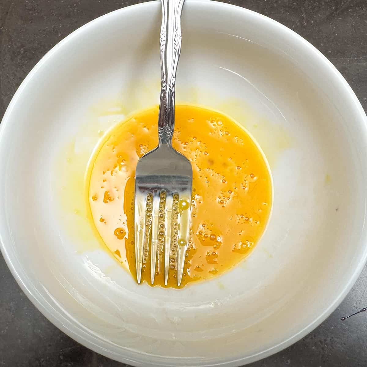 Egg yolk and vanilla extract mixed with a fork in a small bowl.