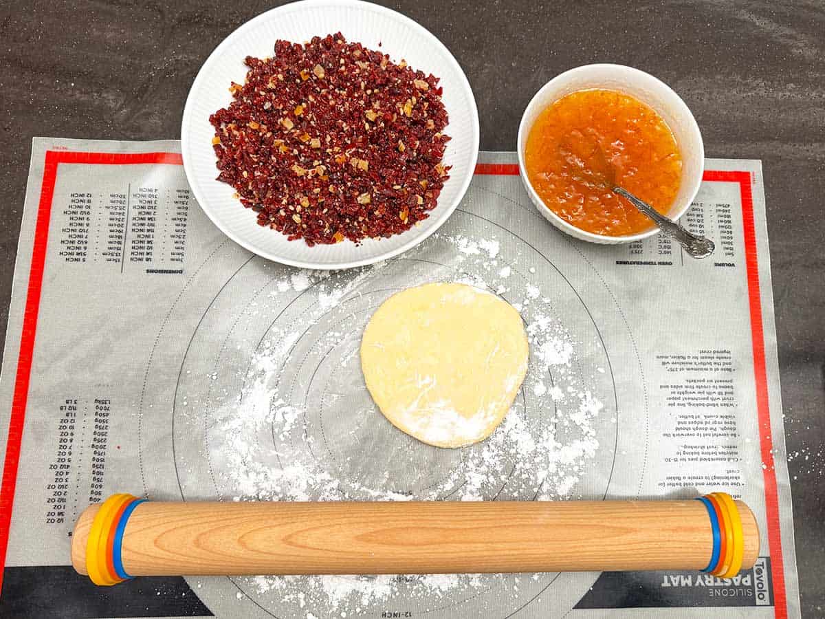 Setup for making the cranberry orange and walnut rugelach with pin, filling, marmalade and dough on dusted pastry sheet.