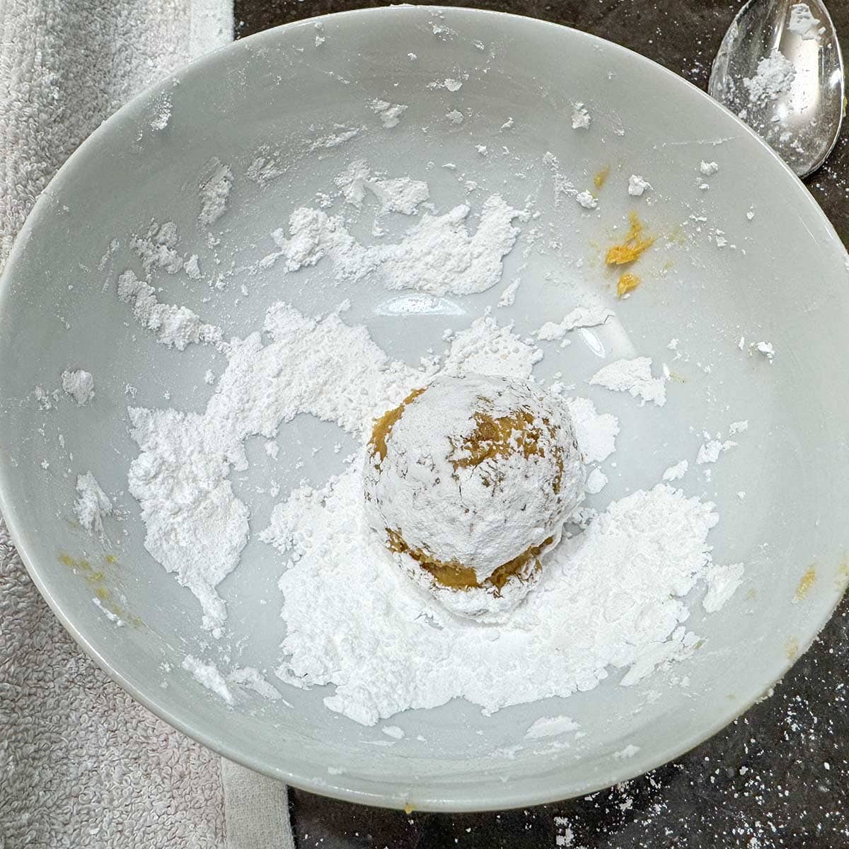 Dropping a spoonful of cookie dough into the powder sugar to get a coating before being baked.